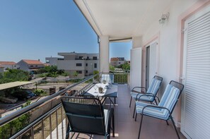 A balcony with a table, chairs, and a car parked outside. - Apartments Dananic (Vodice)