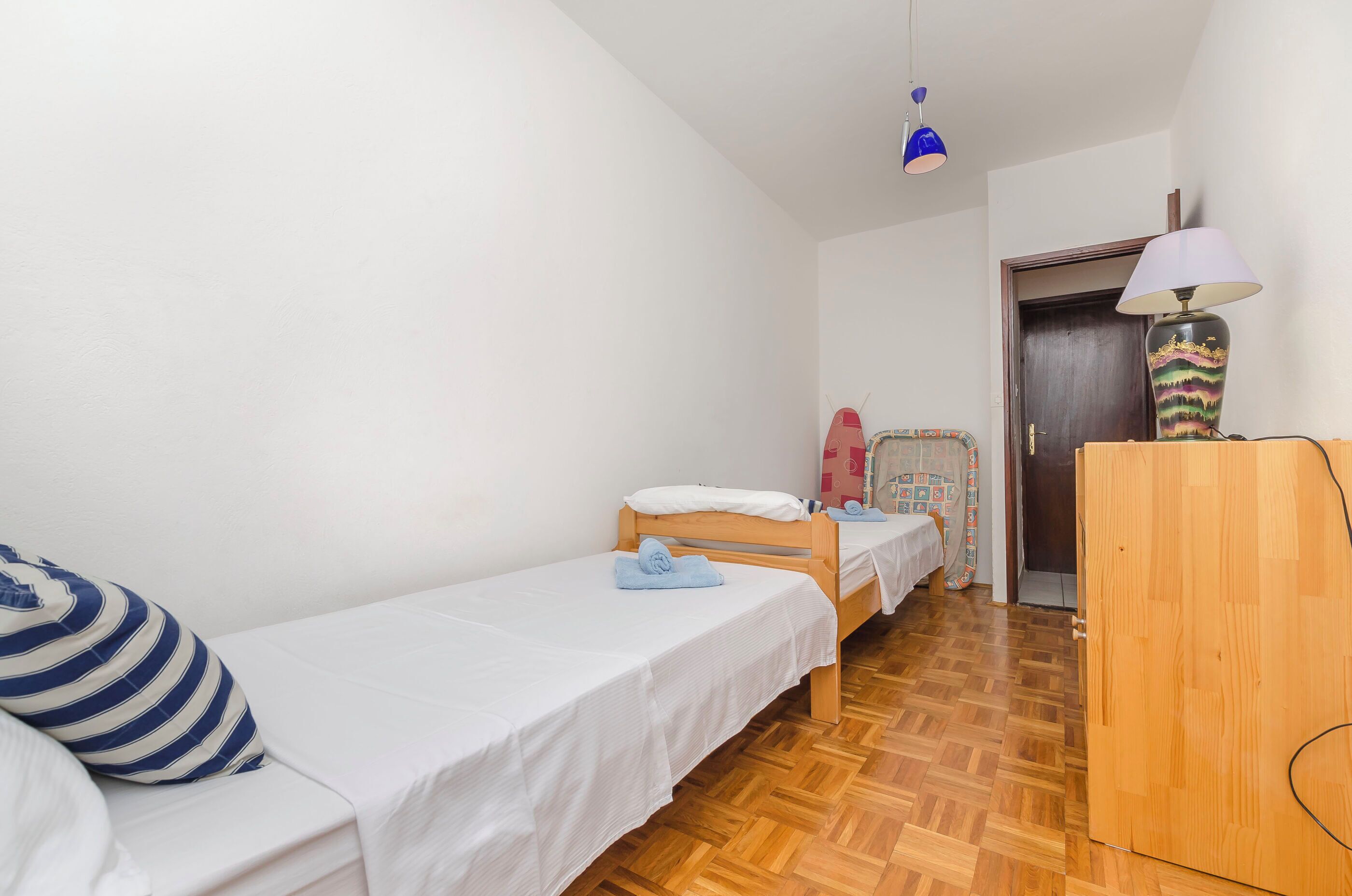 A room with two beds, a wooden wardrobe, a lamp, and a door.