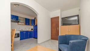 Eine moderne Küche mit blauen Schränken, einem Holztisch, einem blauen Sofa und einem an einem Holzschrank montierten Fernseher.