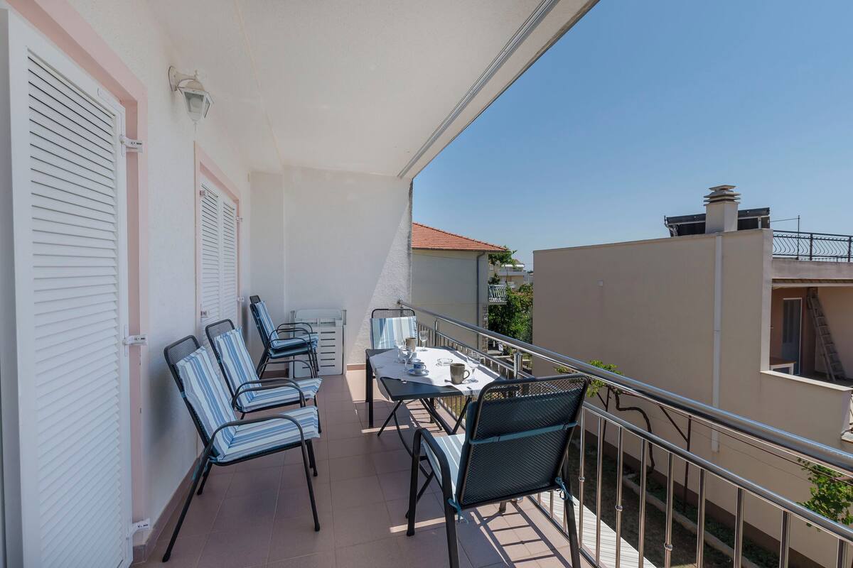 A balcony with a table and chairs, a railing, and a view of adjacent buildings.
