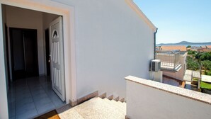 Ein Wohngebäude mit weißer Fassade, einer sichtbaren Tür und einer Treppe, die zu einem Balkon führt.