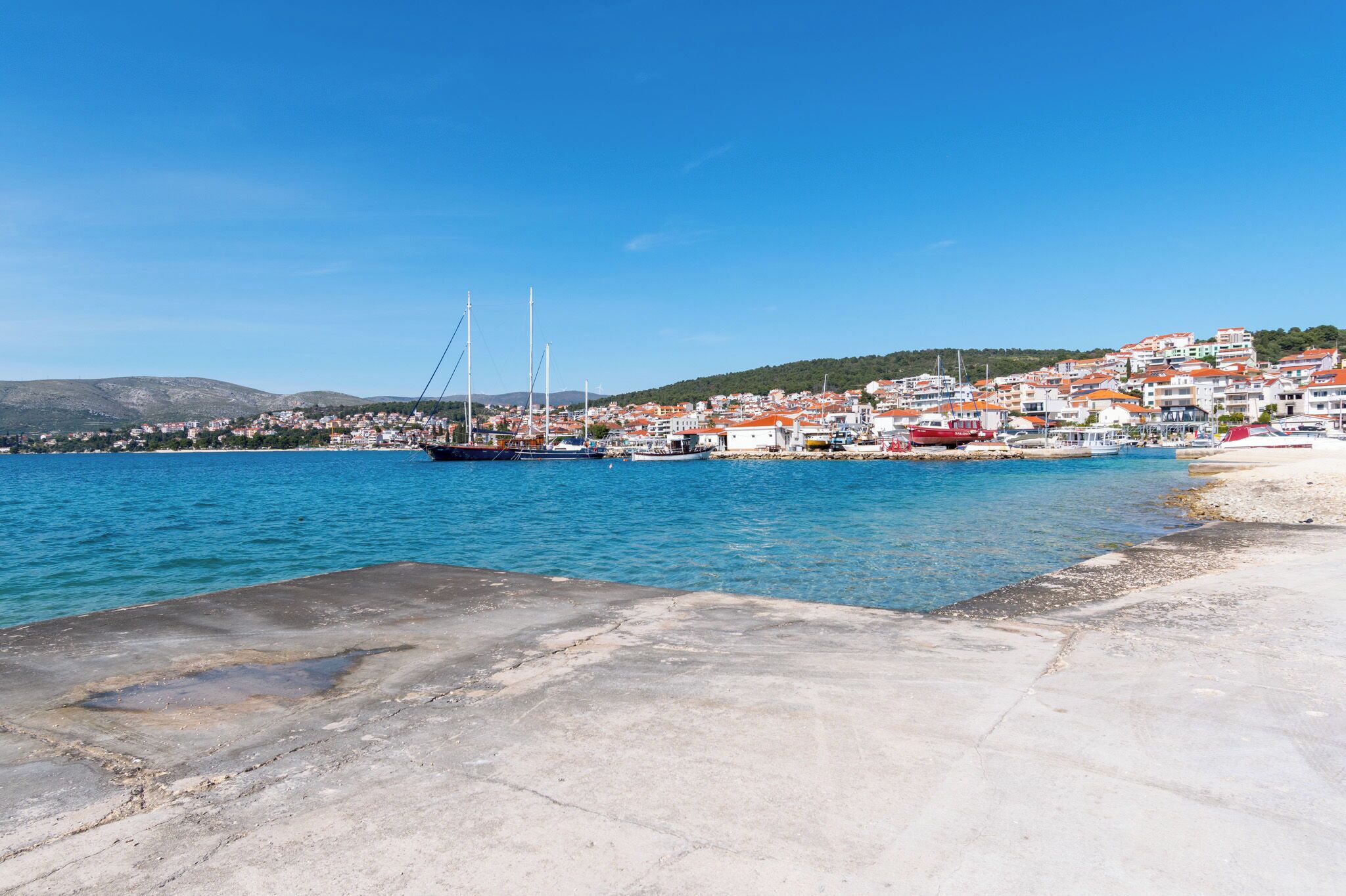 A coastal town with a marina, buildings with red roofs, and a clear blue sky.