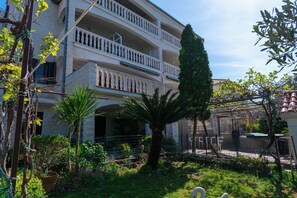 A multi-story building with balconies, a palm tree, and a fenced garden area. - Apartment Maria Stay (Okrug)