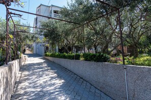 A paved pathway lined with trees and a stone wall, leading to a building with a balcony. - Apartment Maria Stay (Okrug)