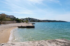 A beach with clear water, a pier, and buildings in the background. - Apartment Maria Stay (Okrug)