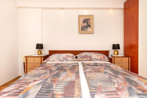 A bedroom with a bed, two bedside tables, a nightstand, a framed picture on the wall, and a wooden headboard. - Apartment Maria Stay (Okrug)
