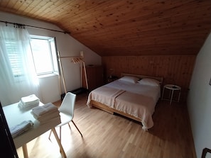 Ein Schlafzimmer mit Holzboden, einem Bett mit weißer Bettwäsche, einem Schreibtisch mit Stuhl und einem Fenster mit Vorhängen.