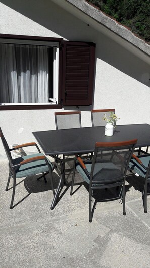 Eine Außenpatio mit Tisch und Stühlen, ein Fenster mit braunen Rollläden und eine weiße Wand.