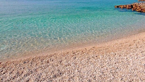 A pebble beach with clear turquoise water and a rocky outcrop.