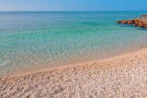 Una playa de guijarros con agua turquesa cristalina y un promontorio rocoso.