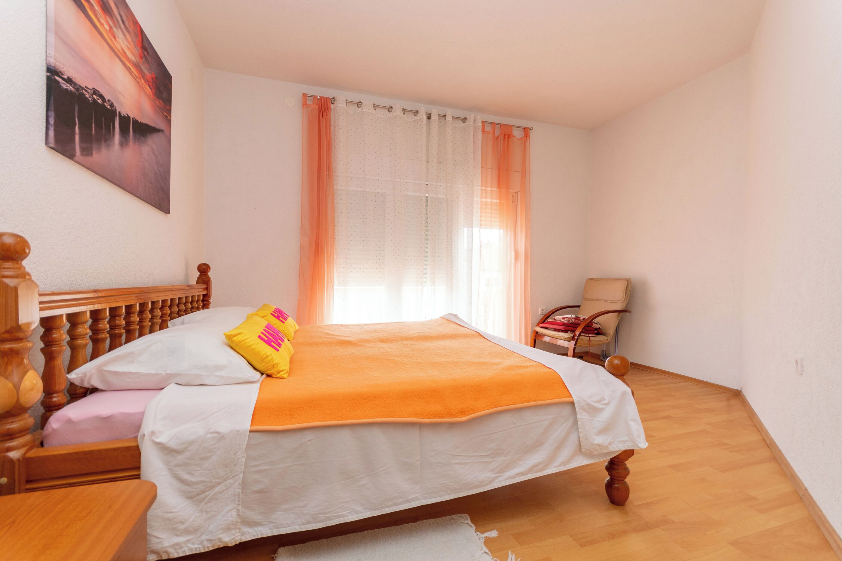 A bedroom with a bed, a chair, a painting on the wall, and a window with curtains.