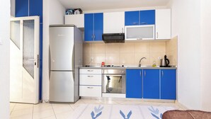 A compact kitchen with blue and white cabinets, a refrigerator, an oven, and a microwave. - Apartments Gardelin in Zadar (Zadar)