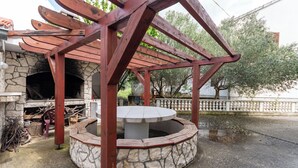 A stone-built outdoor area with a circular stone table, wooden pergola, and a stone oven. - Apartments Gardelin in Zadar (Zadar)