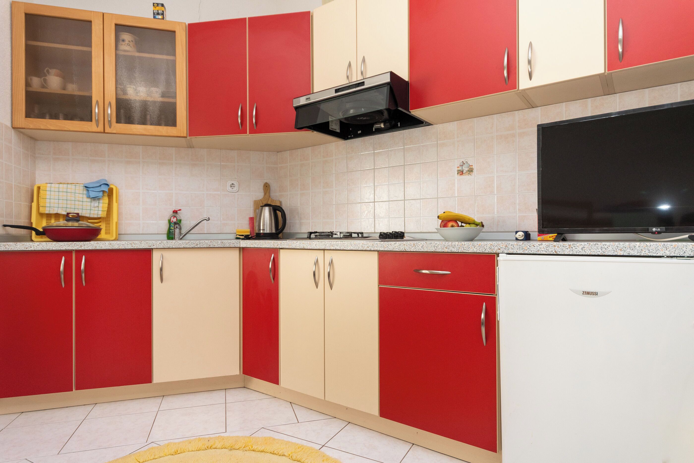 Een keuken met rode en beige kastjes, een fornuis, een magnetron en een vaatwasser.