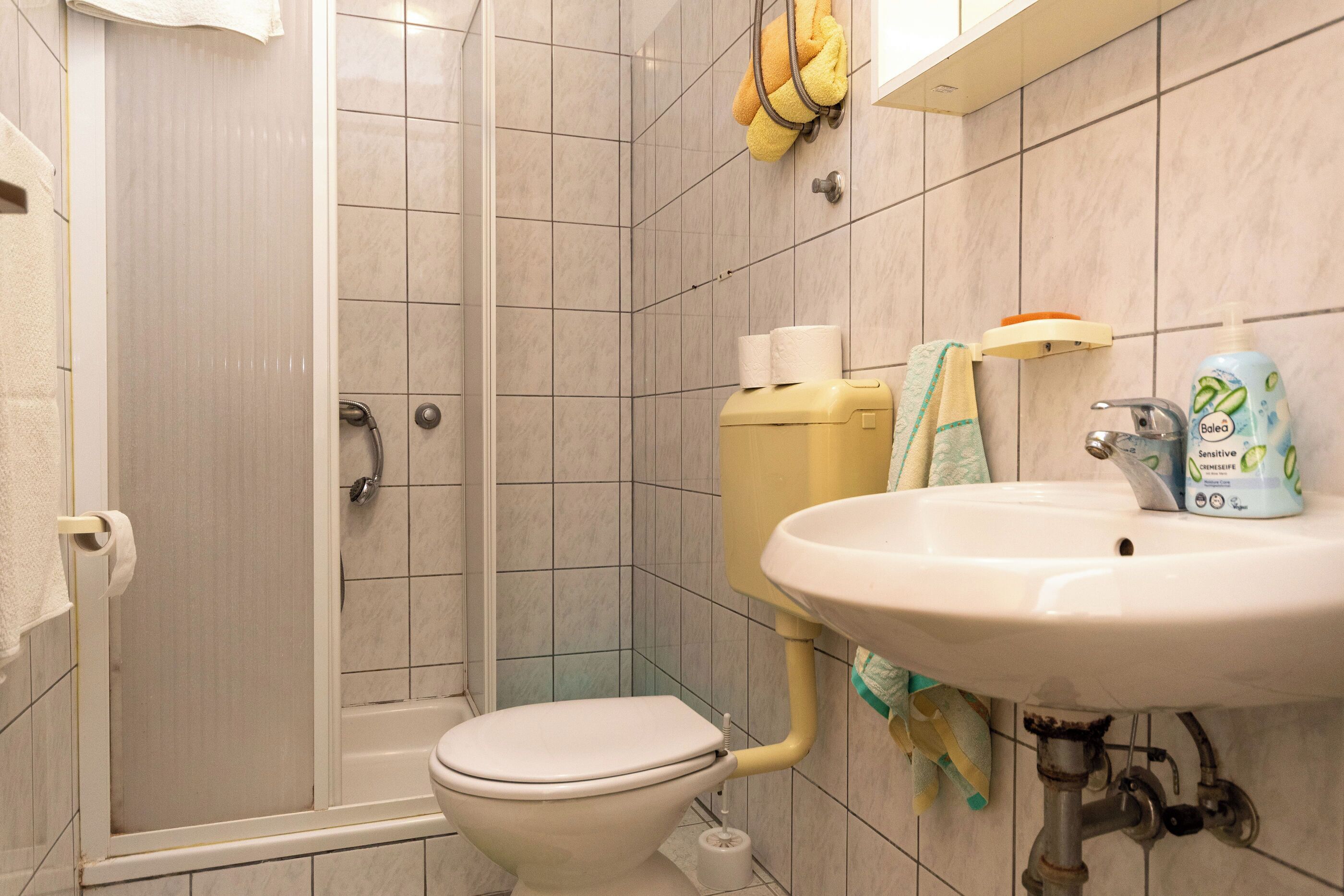 A bathroom with a shower, toilet, sink, and a towel rack with a towel.