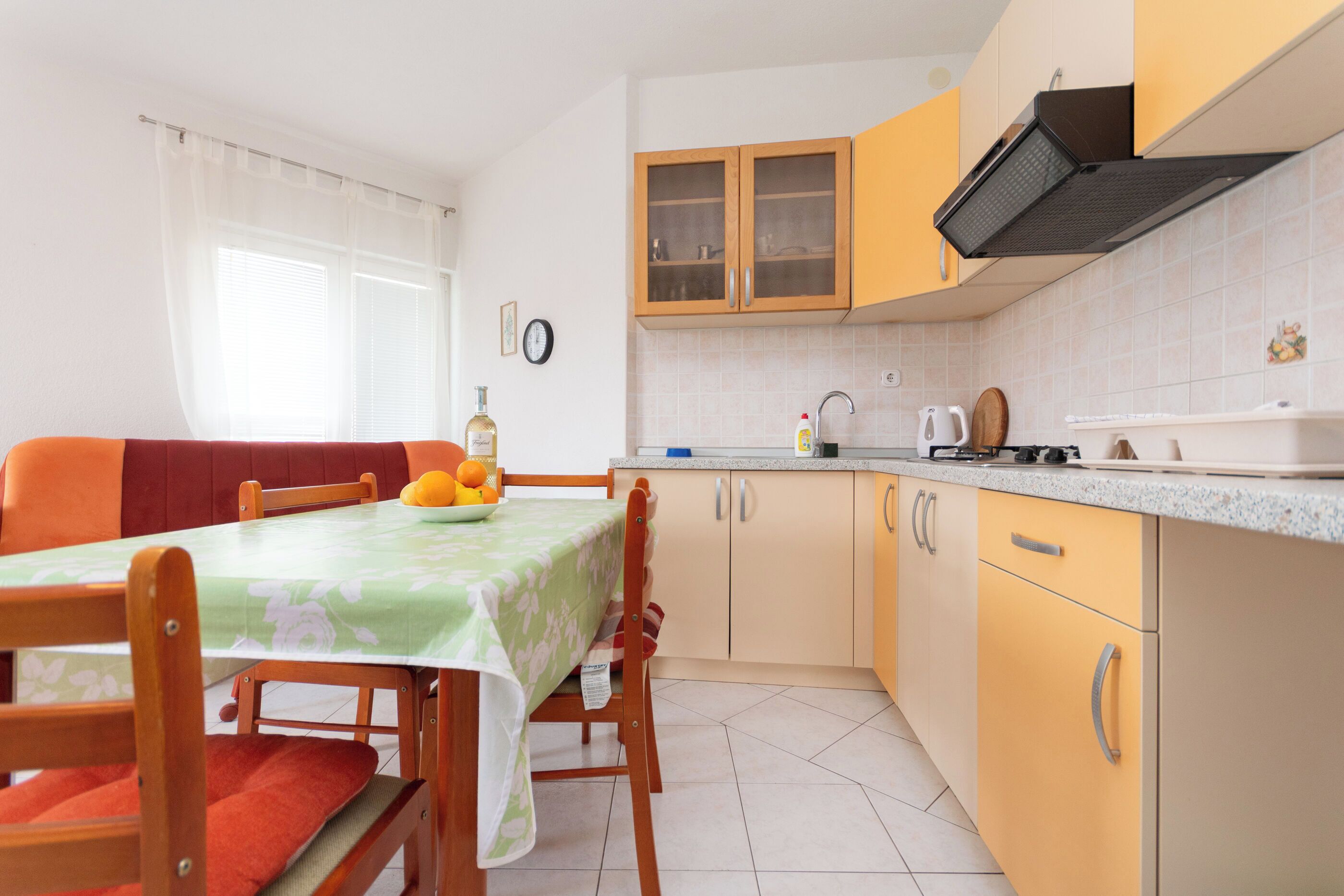 Una cocina con armarios de madera, una mesa de comedor con sillas y un ventanal con cortinas.