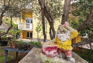 A garden statue of a figure with a hat and a bowl, surrounded by trees and potted plants.