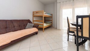 A room with a brown sofa, a wooden bunk bed, a dining table with chairs, and a window with sheer curtains. - Apartments Gardelin in Zadar (Zadar)