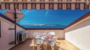 Un porxo cobert amb taula i cadires, vista al mar i un radiador a la paret.