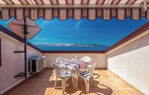 Eine überdachte Terrasse mit Tisch und Stühlen, Blick auf das Meer und ein Heizkörper an der Wand.
