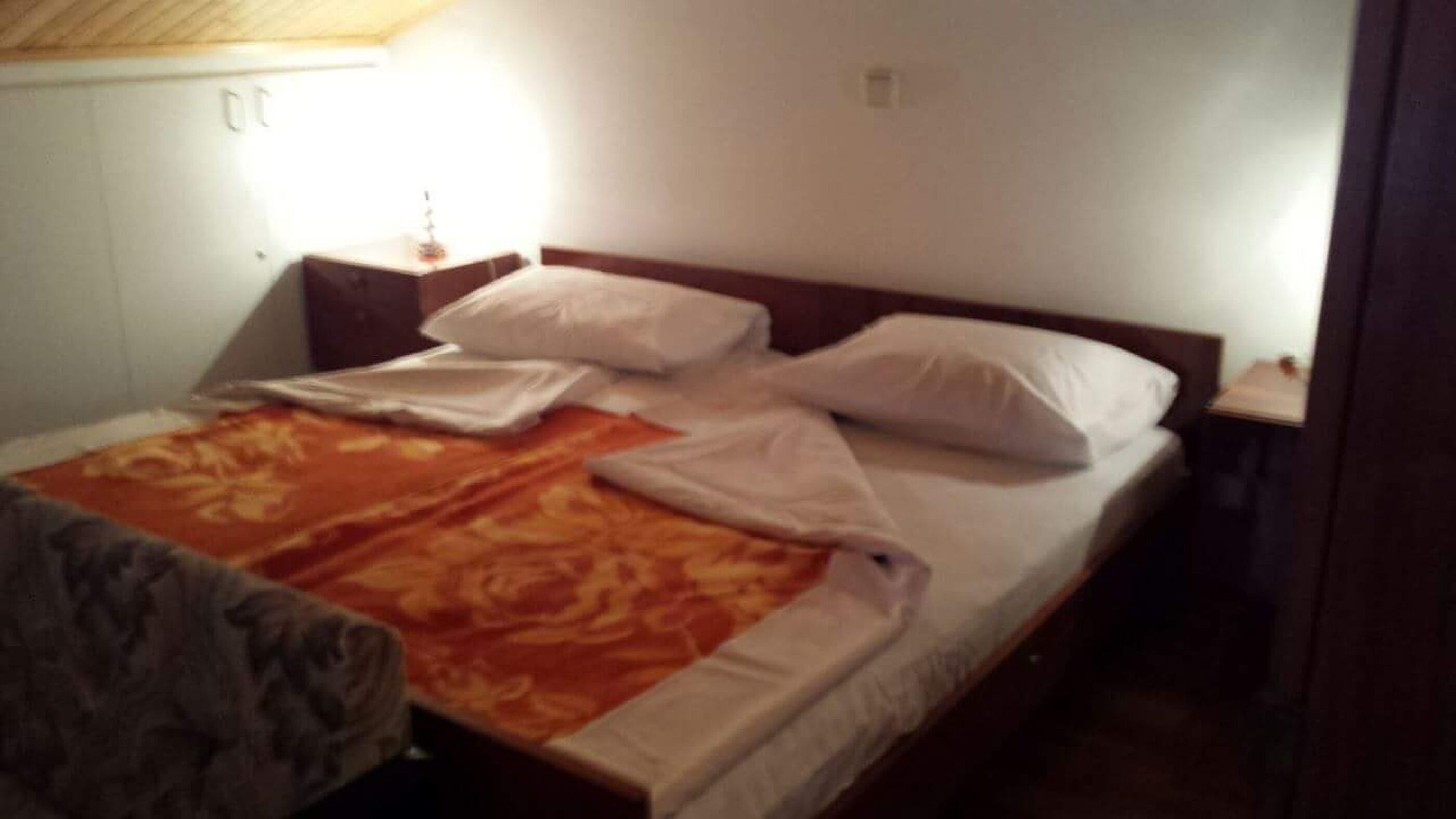 A bed with white linens and a patterned blanket, a bedside table with a lamp, and a wooden headboard.