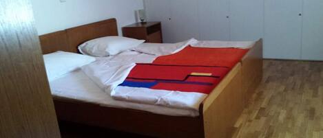 Una cama individual con ropa de cama blanca, una colcha azul y roja, y un cabecero de madera.
