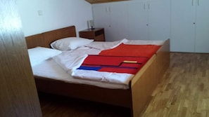 Ein Einzelbett mit weißer Bettwäsche, einer roten und blauen Decke sowie einem Holz-Kopfteil.