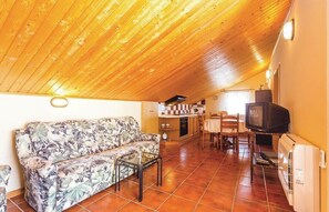 Ein Wohnzimmer mit Holzboden, einer Couch, einem Couchtisch, einem Fernseher und einer Küche im Hintergrund.