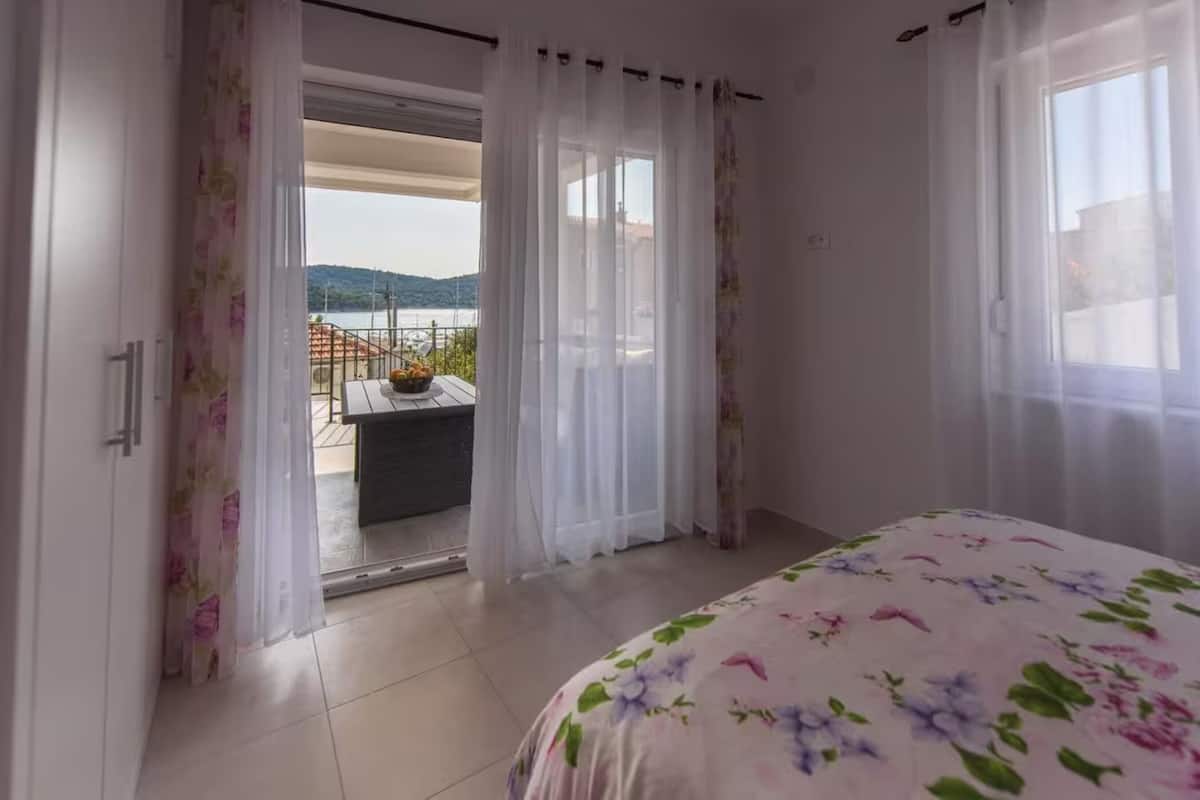 Un dormitorio con cama, un balcón con mesa y sillas, y vistas al exterior.