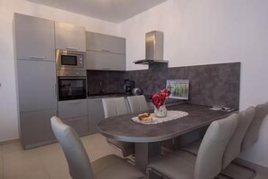 A modern kitchen with built-in appliances, a dining table with chairs, and a decorative vase. - Apartments Guliana Tisno (Tisno)