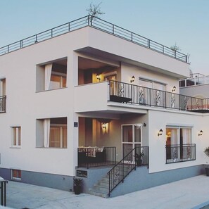 A two-story building with balconies, a staircase, and exterior lighting.