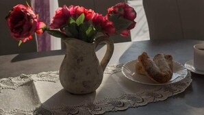 A table with a vase of flowers, a plate with food, and a cup, with a view of a marina and mountains in the background.
