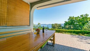 A wooden table with a bottle and glasses, a view of the sea, and a patterned patio. - Apartment Perfect (Omis)