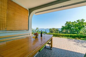 A wooden table with a bottle and glasses, a view of the sea, and a patterned patio. - Apartment Perfect (Omis)