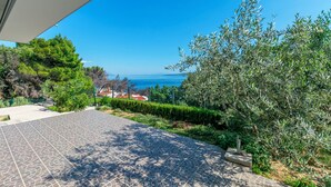 A paved outdoor area with a view of the sea, surrounded by greenery and a building. - Apartment Perfect (Omis)