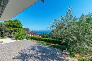 A paved outdoor area with a view of the sea, surrounded by greenery and a building. - Apartment Perfect (Omis)
