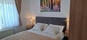 Ein Schlafzimmer mit einem Bett, zwei Nachttischen, einem Wandbild und einem Fenster mit Vorhängen.