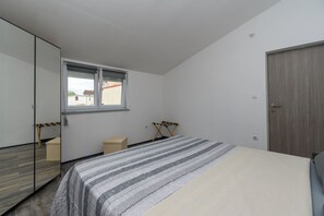 Un dormitorio con cama, ventana, espejo, armario y puerta.