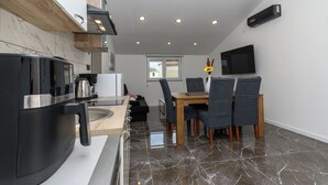 Una cocina moderna con horno integrado, una zona de comedor con mesa y sillas de madera, y un televisor de pantalla plana montado en la pared.
