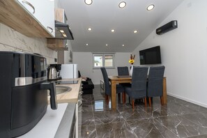Una cocina moderna con horno integrado, una zona de comedor con mesa y sillas de madera, y un televisor de pantalla plana montado en la pared.
