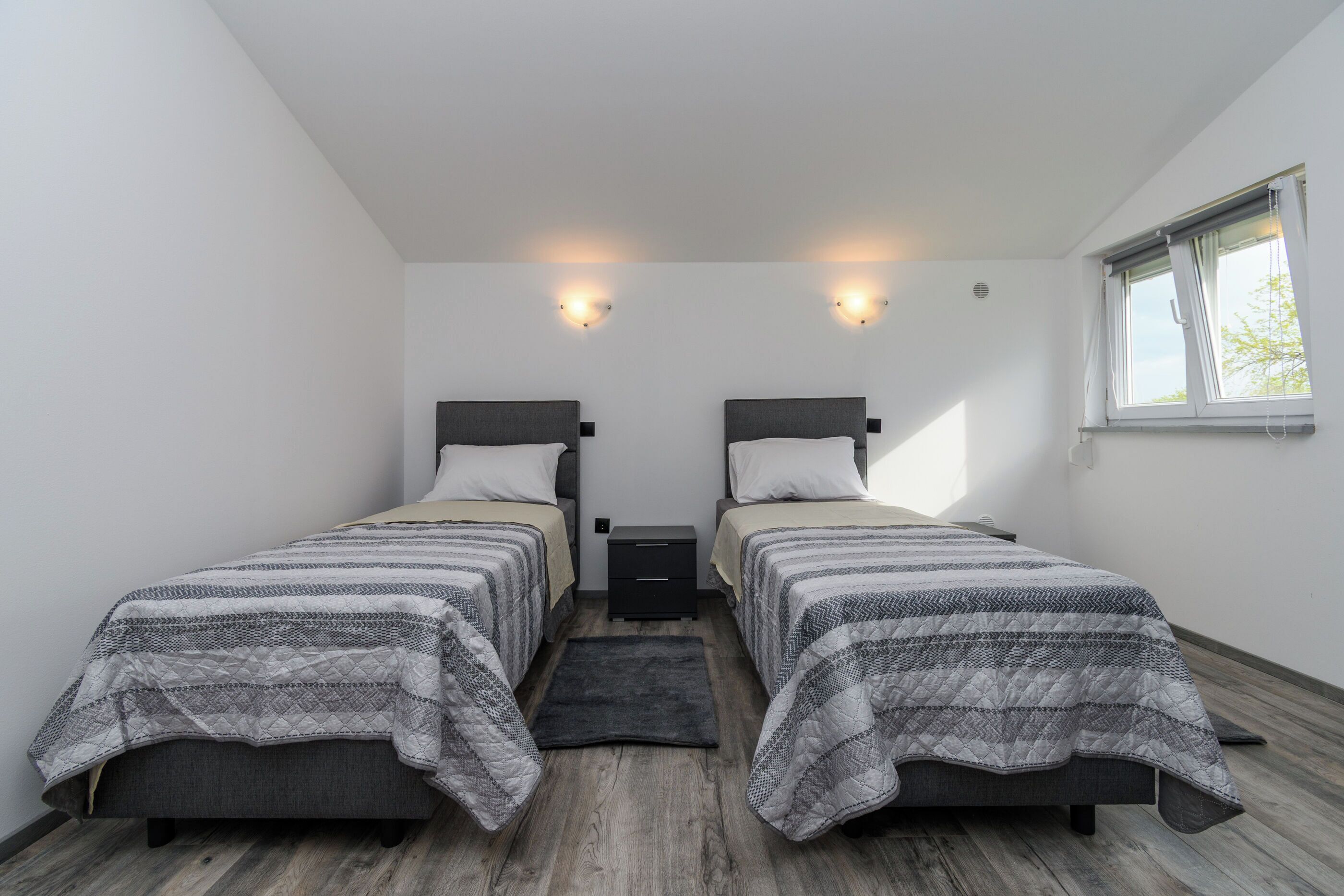 A bedroom with two beds, a small nightstand, a window, and a light fixture.