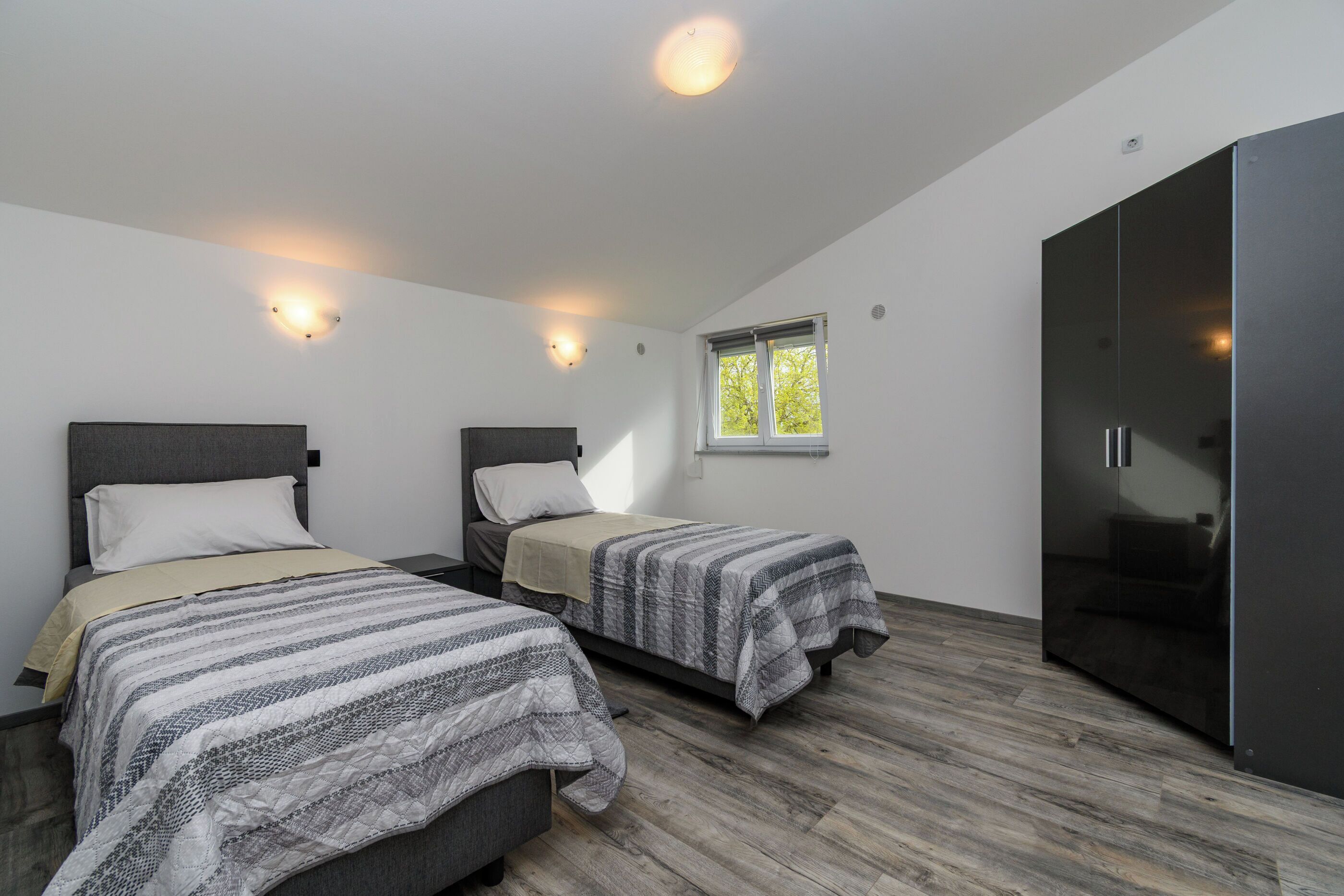 A bedroom with two beds, a wardrobe, and a window.