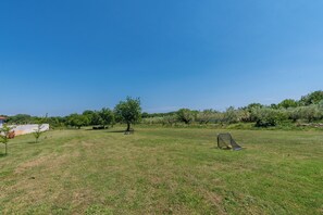 An open grassy field with a soccer goal, trees, and a building in the background.