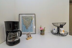 A coffee maker, a framed map, a small flower vase, and a coffee filter basket on a white table.