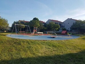 A playground with swings and slides, surrounded by grass and trees, with houses in the background. - Apartment Niko (Pula)