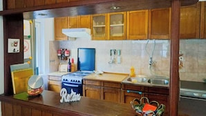 A kitchen with wooden cabinets, a stove, a sink, and a countertop with a jar and a decorative sign. - Apartment Niko (Pula)