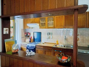 A kitchen with wooden cabinets, a stove, a sink, and a countertop with a jar and a decorative sign. - Apartment Niko (Pula)