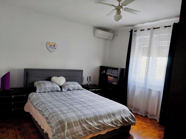 A bedroom with a bed, a ceiling fan, an air conditioner, a TV, and a window with curtains. - Apartment Niko (Pula)