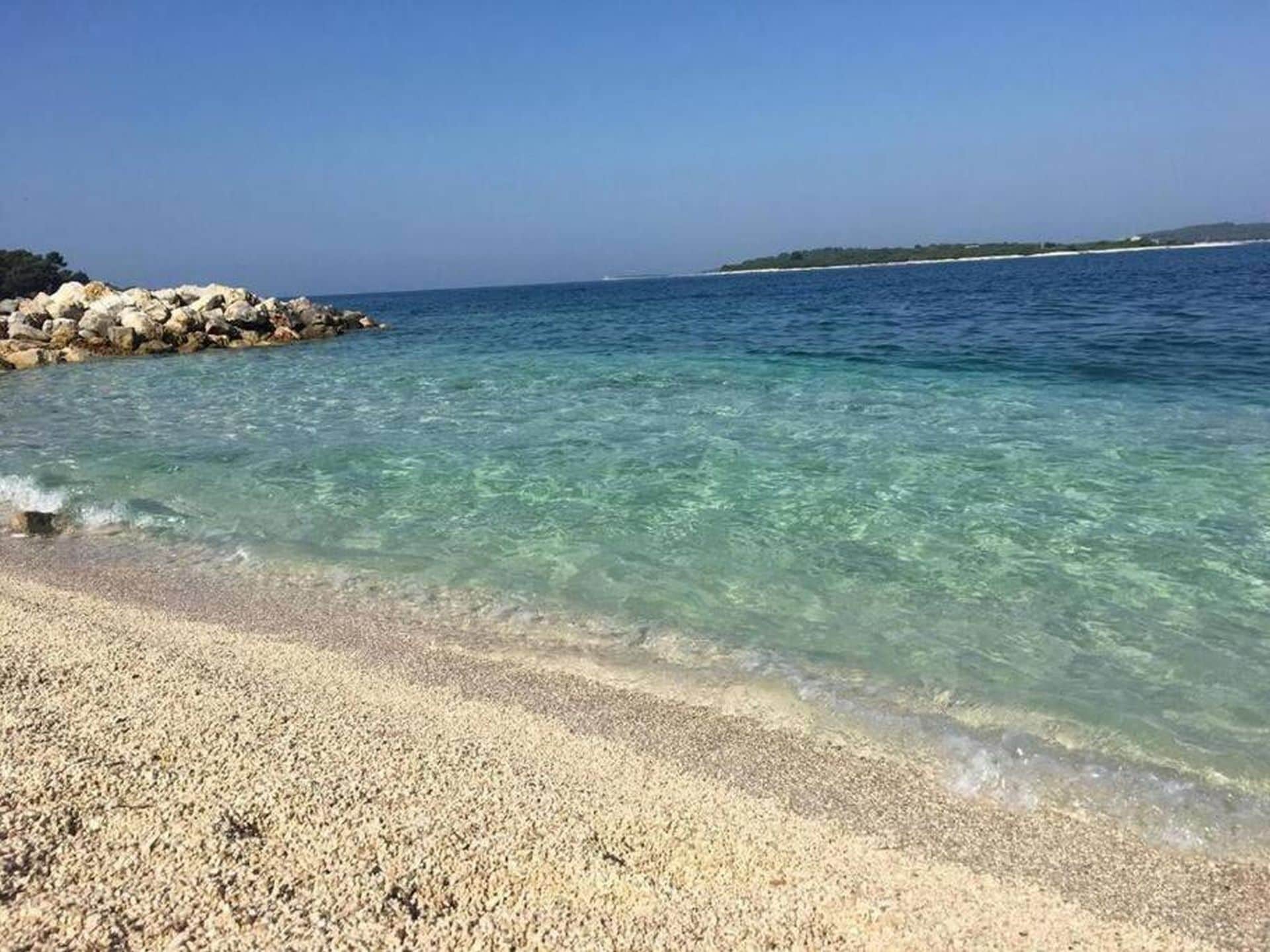A clear beach with pebbles and calm water.