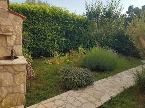 A stone structure with a water feature, a stone pathway, and a variety of plants and shrubs. - Apartment Niko (Pula)